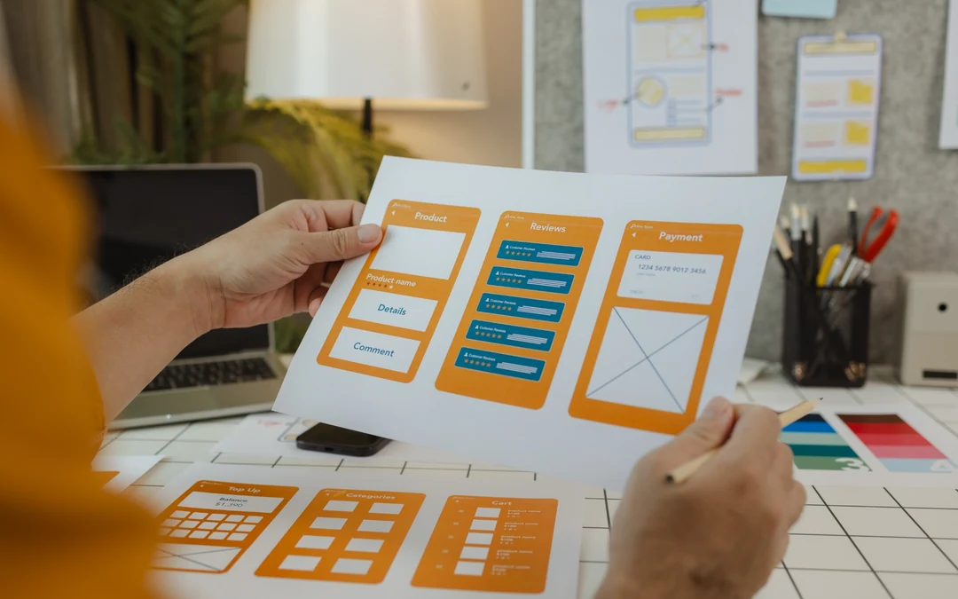Designer reviewing printed mobile interface and form wireframes at a desk