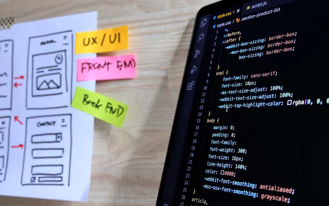 Website wireframes, UX notes, and front-end code displayed on a developer workspace